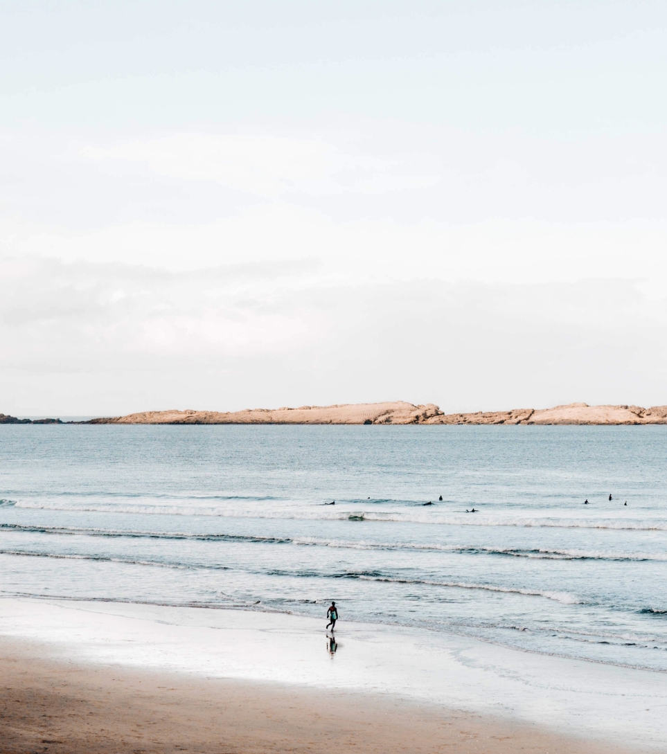 A person strolling along the shoreline, near the water, on a serene beach with golden sand.